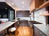 A modern kitchen with dark gray cabinets, marble countertops, and wooden floors. A large window or sliding door opens to an outdoor area with plants. Anteprima dell’immagine prodotto