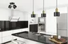 A modern kitchen with black countertops, white cabinets, and stainless steel appliances, featuring several pendant lights and a ceiling spotlight. Produktbild-Vorschau