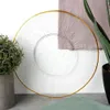 A clear glass plate with a gold rim is shown on a table, with plants and fabric in the background. Podgląd zdjęcia produktu