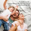 A family is laughing and playing together on a bed. Produktbild-Vorschau