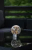 A solar-powered LED light sits on a reflective surface, with outdoor furniture in the background. Produktbild-Vorschau