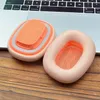 Two orange ear pads for headphones are placed on a wooden surface next to a laptop. Produktbild-Vorschau