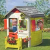 Two children playing in a Smoby Neo Jura Lodge playhouse in a garden. Produktbild-Vorschau