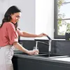A woman is filling a glass with water from a kitchen faucet. Produktbild-Vorschau