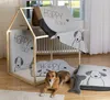 A dog is lying in front of a wooden dog house with blankets and pillows inside and around it. Produktbild-Vorschau