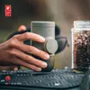 A hand holding a portable espresso maker next to a jar of coffee beans. Produktbild-Vorschau