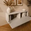 A wall-mounted cabinet with its door open, displaying books and decorative items. The cabinet is mounted on a wall with framed art above it, and a wooden floor below. Náhľad obrázku produktu