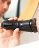 A man is shaving his face with an electric razor in front of a mirror. Voir les images du produit
