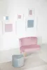A pink velvet children's sofa and a heart-shaped light blue ottoman are placed against a white wall with framed artwork. Voir les images du produit