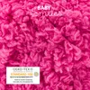 A close-up of fluffy pink yarn with text overlays and a certification logo. Produktbild-Vorschau