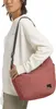 A person wearing a cream sweatshirt and holding a red bag. Produktbild-Vorschau
