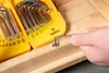 A hand is using a hex key to tighten a screw in a wooden surface, with a set of hex keys in a yellow case in the background. Anteprima dell’immagine prodotto