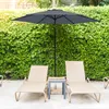 Two lounge chairs and a patio umbrella are set up on a patio next to a lush green hedge. Produktbild-Vorschau