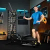 A man is posing next to a TREX SPORT Crosstrainer in a home gym setting. Produktbild-Vorschau