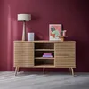 A wooden sideboard with slatted doors is displayed against a deep red wall, with a lamp, artwork, and decorative items on top. Anteprima dell’immagine prodotto