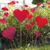 Red heart-shaped decorations are placed in a garden with roses and green foliage. Produktbild-Vorschau