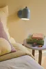 A bedside scene with a wall lamp, pillows, and books on a small table. Voir les images du produit