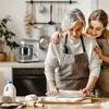 An older woman and a younger woman are in a kitchen, baking together. The older woman is rolling out dough with a rolling pin, and the younger woman has her arms around her. Produktbild-Vorschau