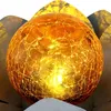 A close-up of a decorative cracked glass orb with internal lighting, possibly a solar garden light, set within metallic petal-like structures. Produktbild-Vorschau