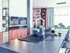 A modern kitchen with a sink and faucet in the foreground, and a living/dining area in the background. Produktbild-Vorschau