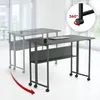 Two desks are shown in a bright, modern office or home setting. The foreground desk is dark gray and in focus, while the background desk is a lighter gray and blurred, suggesting movement or a different position. A red arrow indicates rotation or movement. Produktbild-Vorschau