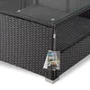 A close-up view of the corner of a black rattan outdoor furniture set with a glass top, showing a product tag hanging from it. Produktbild-Vorschau