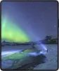 A person with a flashlight illuminates the aurora borealis over a snowy landscape. Produktbild-Vorschau