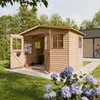 A wooden garden shed with its doors open, showing a scooter and other items inside, set in a grassy yard with flowers in the foreground and a modern building in the background. Náhled obrázku produktu