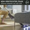 A person is vacuuming under a piece of furniture with a cordless vacuum cleaner that has LED lights on the nozzle. Produktbild-Vorschau