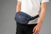 A person wearing a white t-shirt and black pants is shown from the waist down, with a navy blue hip pack around their waist. Produktbild-Vorschau