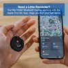 A person is holding a black Bluetooth tracker and a smartphone displaying a map. Podgląd zdjęcia produktu