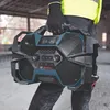 A person wearing work clothes and gloves holds a rugged radio on a construction site. Produktbild-Vorschau