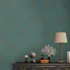 A close-up of a dark dresser with decorative items on top, including a lamp, globes, and books, against a patterned teal wallpaper. Produktbild-Vorschau