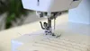 A close-up shot of a sewing machine needle and foot stitching a wavy line on fabric. Produktbild-Vorschau
