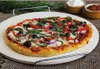 A pizza on a pizza stone, with some ingredients in bowls in the background. Podgląd zdjęcia produktu