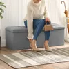 A woman sits on a storage bench in a hallway, holding a small purse.