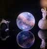 A galaxy-themed moon lamp is displayed on a reflective black surface, with a vintage Nikon camera and an astronaut figurine as props. Náhľad obrázku produktu