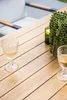 A close-up of a wooden table with two glasses of white wine and a potted plant. Produktbild-Vorschau