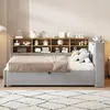 A light gray upholstered bed with a wooden headboard shelf filled with decorative items, placed in a room with a patterned rug and a floor lamp. Podgląd zdjęcia produktu