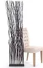A decorative room divider made of dark, wavy branches stands next to a beige upholstered chair against a white background. Náhled obrázku produktu