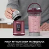 A person is holding the lid of a blender over the base, with a blender cup filled with a pink smoothie to the right. Podgląd zdjęcia produktu
