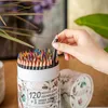 A hand is holding a colored pencil from a large set of colored pencils in a cylindrical container. Produktbild-Vorschau