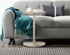 A side table with a blanket, book, and cup of coffee next to a sofa. Produktbild-Vorschau