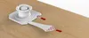 A white plastic mounting bracket with red arrows indicating movement, placed on a light brown wooden surface. Produktbild-Vorschau