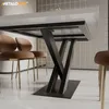 A close-up view of a modern dining table with a black X-shaped metal base and a white tabletop, surrounded by plush brown chairs with gold legs. Podgląd zdjęcia produktu