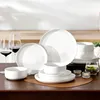 A set of white ceramic dishes and wine glasses are arranged on a wooden table. Produktbild-Vorschau