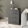 A gray nightstand with three drawers is placed next to a sofa in a room with a plant and a lamp on top of the nightstand. Voir les images du produit