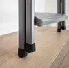 Close-up view of the bottom of a metal step stool with rubber feet on a wooden floor. Voir les images du produit