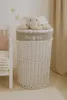 A plush elephant toy sits atop a white wicker laundry basket in a nursery or child's room. Podgląd zdjęcia produktu