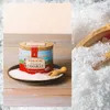 A tin of Fleur de Sel salt sits on a bed of salt, with a small wooden scoop, on a wooden surface. The background is split between a light, textured surface and a pile of salt with a wooden scoop. Voir les images du produit